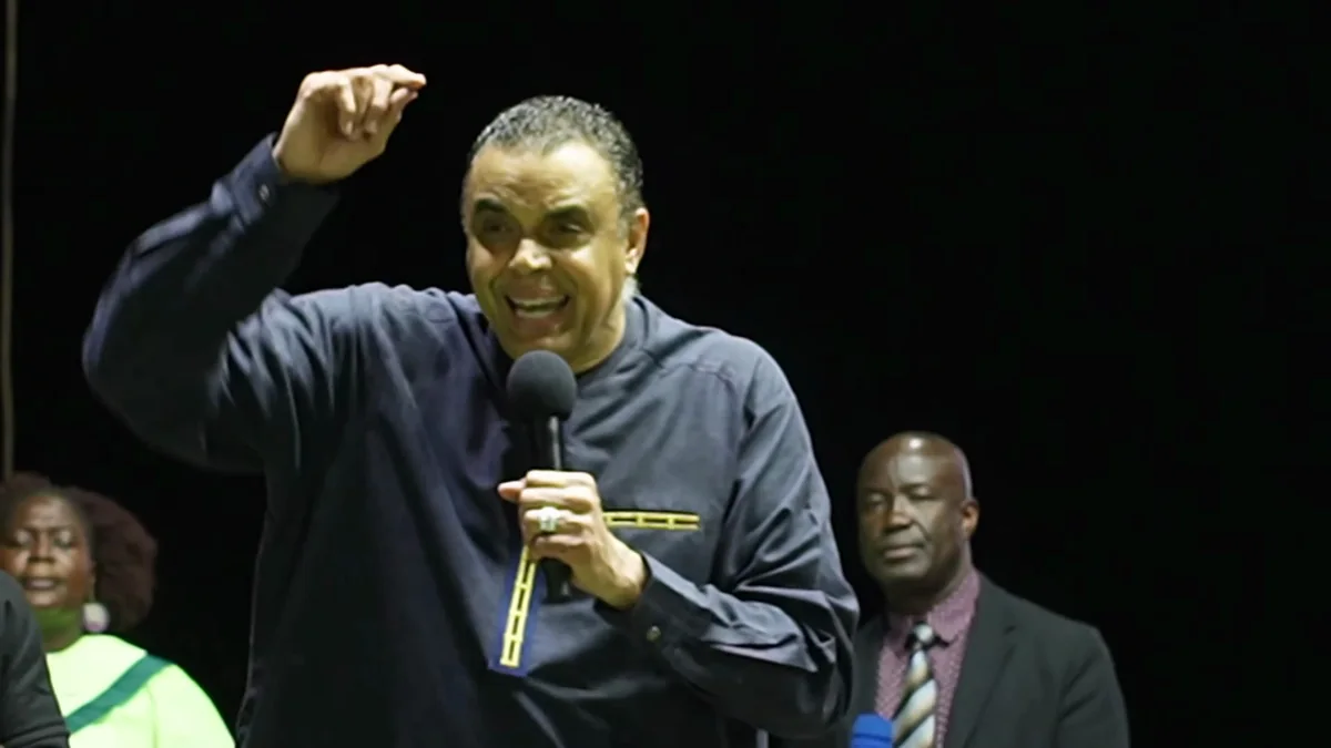 Bishop Dag Heward-Mills smiling broadly with a fist raised in celebration on a crusade stage at night.