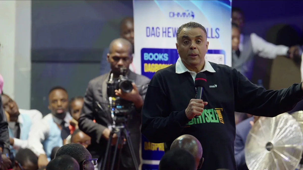 Bishop Dag Heward-Mills teaching in a conference hall beside a stand of his books