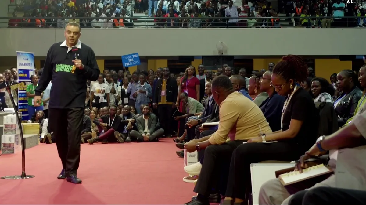 Bishop Dag Heward-Mills on a red stage addressing a packed conference hall with balconies in Kampala.
