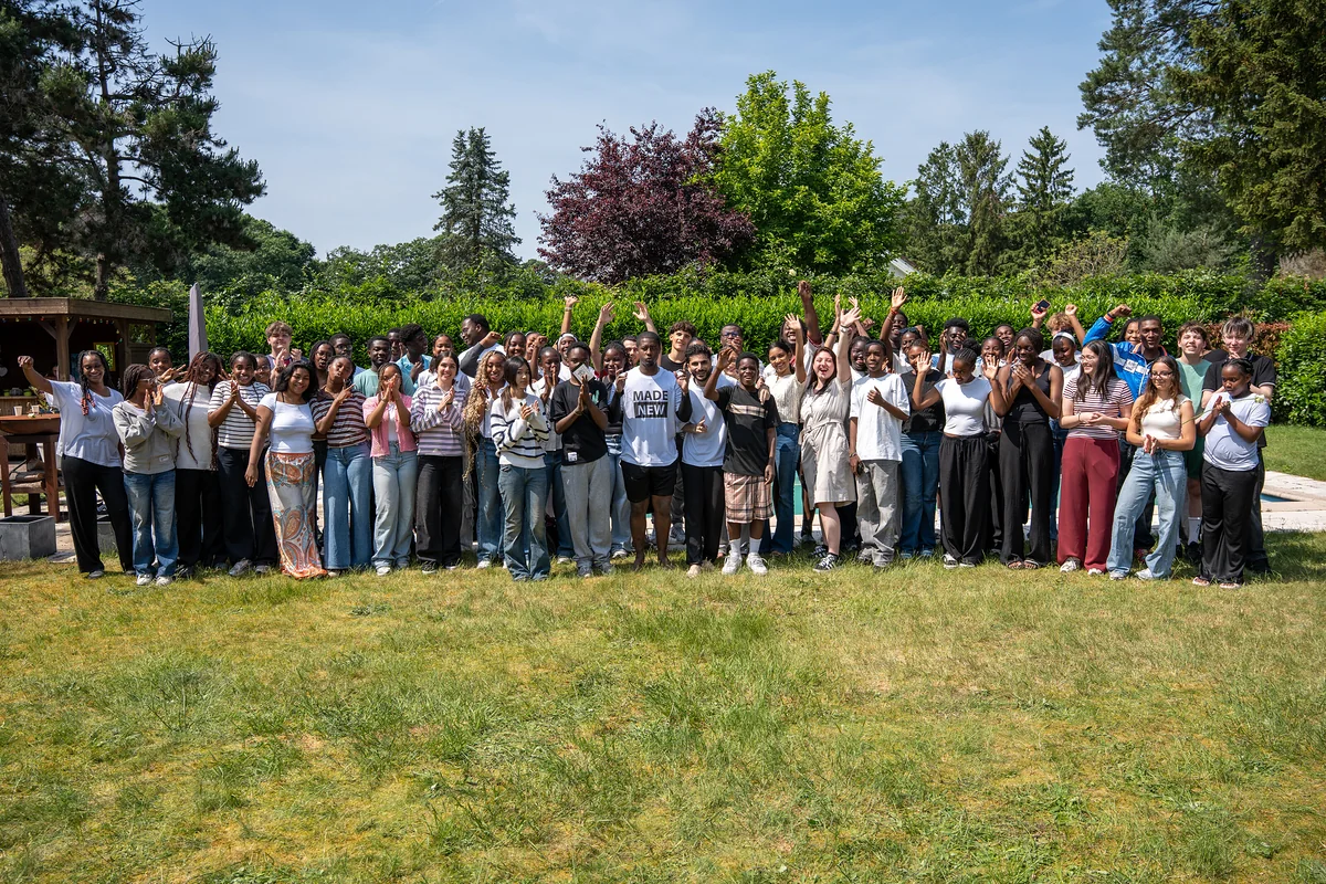 About a hundred young adults cheering and waving for a group photo on a garden lawn on baptism day.
