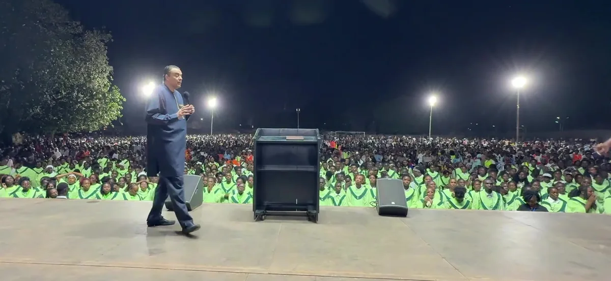 Bishop Dag Heward-Mills walks across a floodlit stage towards a crowd of thousands at night in Banjul, The Gambia.
